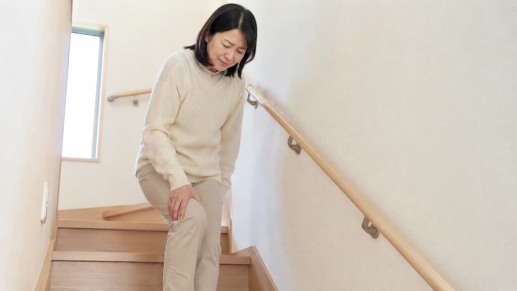 階段の上り下りで膝の痛みを感じて手を押さえる女性のイメージ